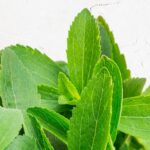Fresh stevia leaves and small bowl with sugar on a white wooden table.