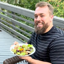 Bearded gentleman, Wes Schweitzer, holding a plate of fresh greens sitting on an outdoor patio.