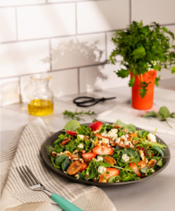 A delectable plate of food rests on a table, showcasing a vibrant salad. In the background, a pink ySleeve holding a mustard plants adds a touch of flavor.