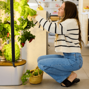 Woman kneeling next to a Gardyn Home, harvesting vegetables.